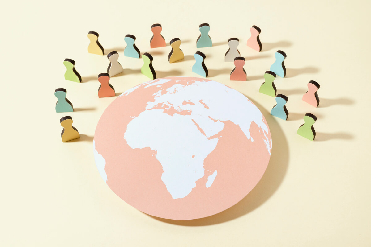 cardboard silhouettes of people in pastel colors arranged around a globe in front of a yellow background