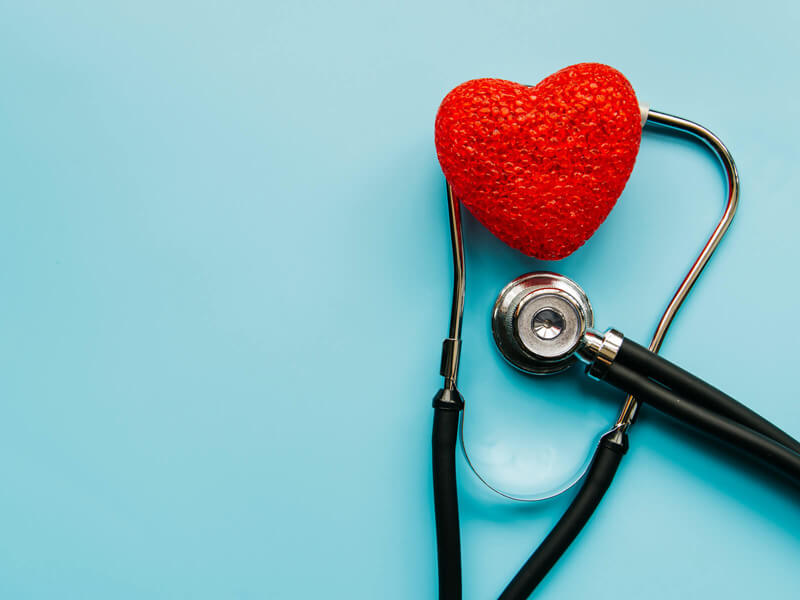 doktorski stetoskop postavljen oko crvenog srca, postavljen preko svetlo plave pozadine